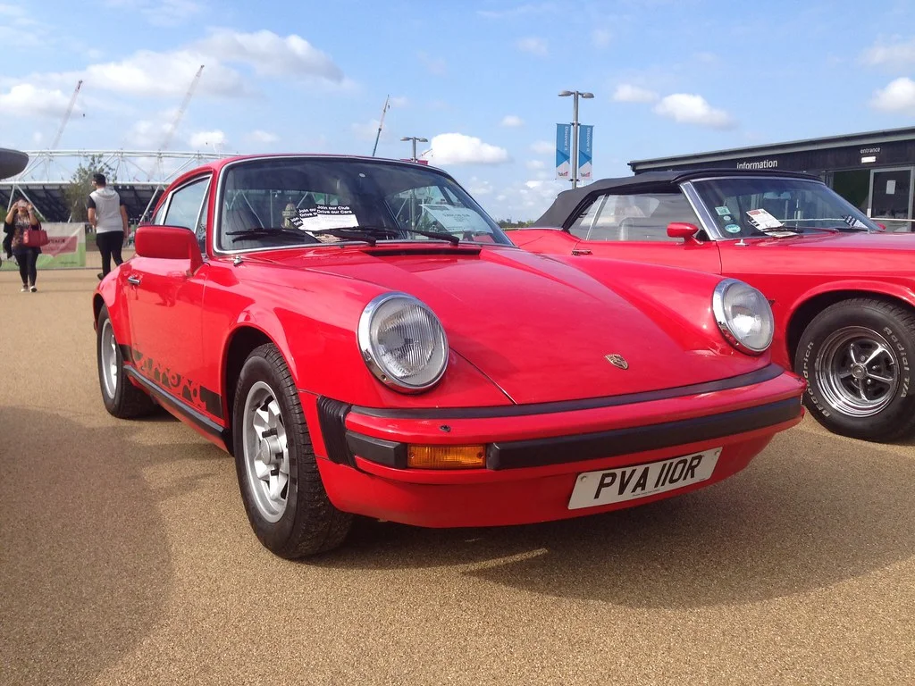 A classic Porsche 911 at a car show, with its sloping roofline and rounded rear engine shape in view.