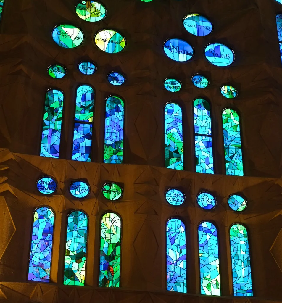 Interior of the Sagrada Família with blue and green stained-glass light rising through the columns.
